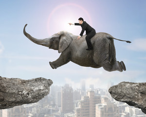 Man with pointing finger riding elephant flying over two cliffs