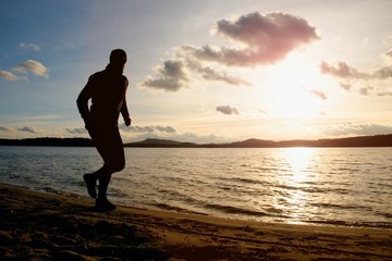 Fototapeta na wymiar Tall man with sunglasses and dark cap is running on beach at autumn sunset