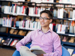 Happy male student holding books at the library