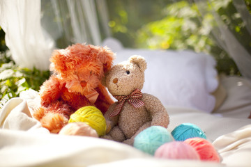 Два плюшевых медведя сидят на кровати рядом с клубками разноцветной пряжи