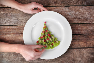 Woman making Christmas fir tree made from kiwi on old wooden table