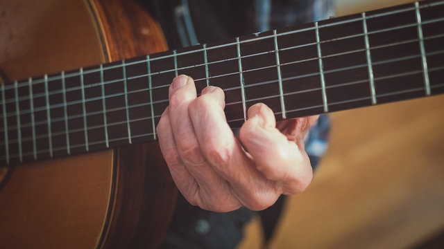 An old man (senior citizen luthier) with aged hands is playing / grabbing a chord on a classical (acoustic) guitar. Close up of the fretboard and the fretting hand.