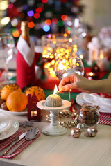 Woman hand lights a candle on holiday table setting