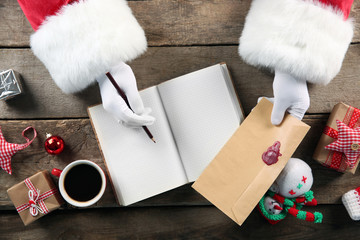 Christmas concept. Santa Claus hands write in notebook on wooden background