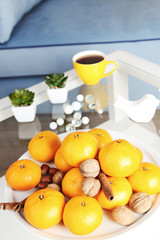 Plate with fresh tangerines on table in living room, close up