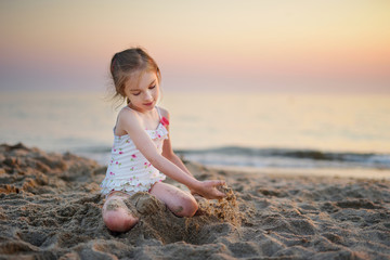 Fototapeta na wymiar Cute little girl having fun with the sand on a evening beach