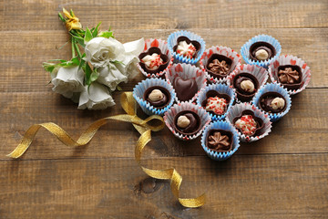 Set of chocolate candies forming heart on a wooden background
