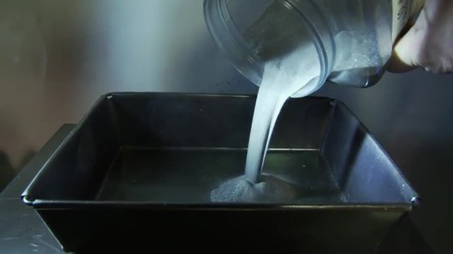 Detail of carbide powder being poured from a plastic bottle into a metal dish.