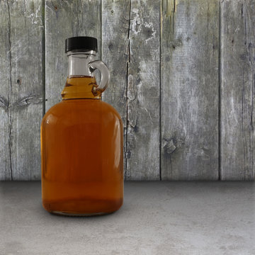 Jug of maple syrup in front of a weathered wood wall