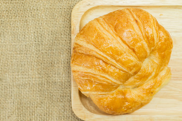 butter croissant on wooden plate on gunny sack texture, top view with copy space