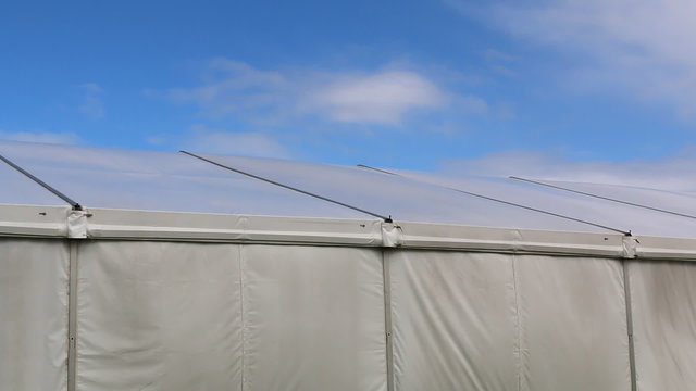 Wind moving canvas of the big social or commercial event tent with blue sky and some white clouds above