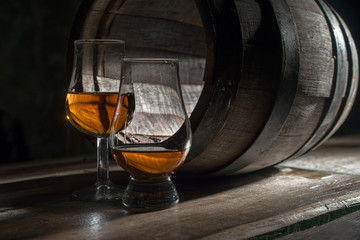 Two glasses of strong alcohol, amid oak barrels
