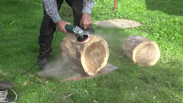 Man hand with electric sander tool sand wooden oak tree log. Carpenter man making decorative chair. Static closeup shot. 4K