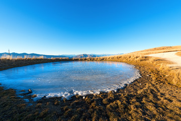 Alpine Frozen Pond - Lessinia Italy / Small alpine frozen pond used in summer for watering the cows that graze on the meadows. Prealps of Veneto, Lessinia, Verona, Italy