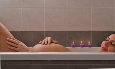 Embarazada relajada en la tina de bañera de un spa con velas.
