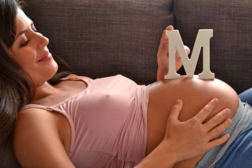 Mujer latina embarazada recostada acariciando barriga y juguete.