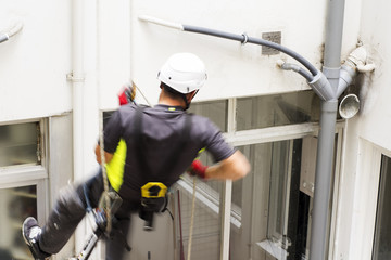 vertical worker  in motion on courtyard  with safety system for repair pipes
