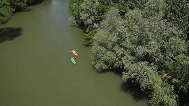 Aerial view of two kayakers paddling down the river surrounded with forest.
