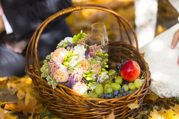 Fototapeta na wymiar Корзинка для пикника с букетом невесты, зеленым и черным виноградом, яблоком и бокалами