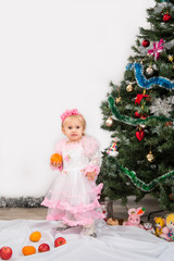 Little girl near the Christmas tree eats mandarins