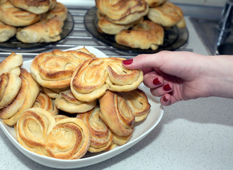 Woman takes tasty appetizing baked bun with crispy ruddy crust from the plate on the table in kitchen