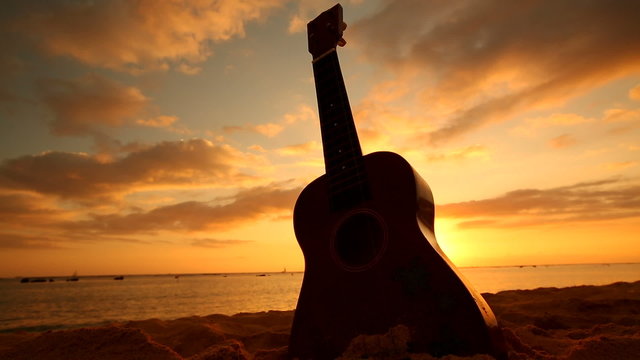 Traditional Hawaiian instrument Ukulele on sandy beach at sunset on Oahu Hawaii.