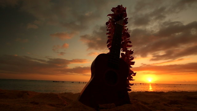 Traditional Hawaiian instrument Ukulele and flower wreath or garland lei on sandy beach at sunset Oahu Hawaii.