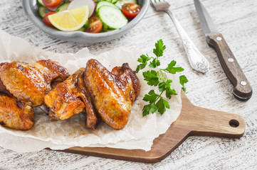 Spicy chicken wings and fresh vegetable salad on wooden white background