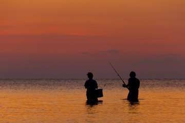 Two fisherman staying in the sea on a tropical island at the sunset 