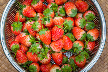 Fresh Strawberries with bright red berries in the stainless steel basket on a wood weave background