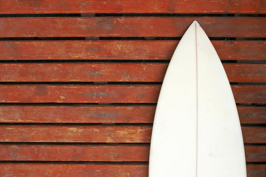 Wei&szlig;es Surfbrett vor roter verwitterter Holzwand