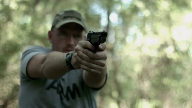Close, frontal view of man firing a .44 caliber pistol in woodland.  Muzzle flashes visible.  Recorded in 4K, Ultra High Definition.