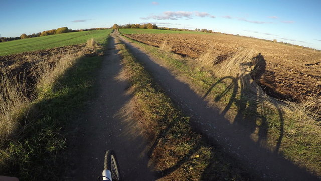 View shot from bicycle going on country road on sunny evening day with bicyclist's shadow, 4K
