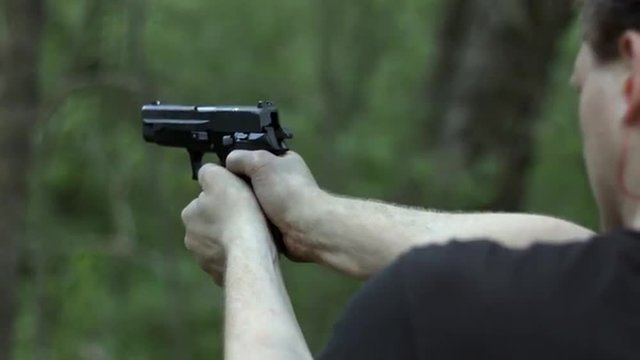 Camera tilts up to a close, over the shoulder view of man firing a .44 caliber pistol in woodland.  Muzzle flashes visible.  Originally recorded in 4K, Ultra High Definition.