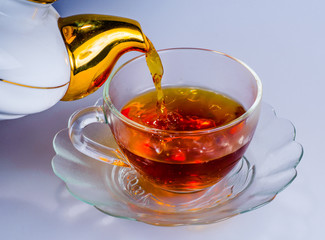 Fresh, fragrant tea/In a transparent glass Cup filled with tea. From the spout of a teapot pouring a stream of beverage.