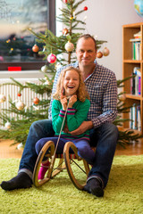 father and daughter together on sled in frontof christmas tree