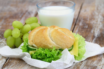 School lunch consisting of cheese roll, grapes and glass of milk
