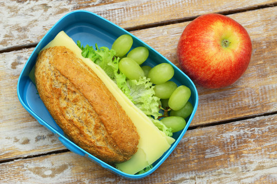 Healthy lunch box containing whole grain bread roll with cheese and lettuce, grapes and apple
