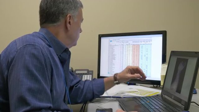A mature man looking at xray images from a canine on his laptop computer screen compares those with data he has on a larger monitor.