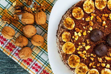 Chocolate cake with nuts and bananas on a plate and walnuts on a yellow napkin