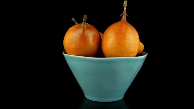 Passion fruit maracuja granadilla on ceramic blue bowl, black background.