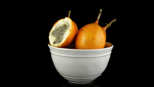 Passion fruit maracuja granadilla on ceramic white bowl, black background.