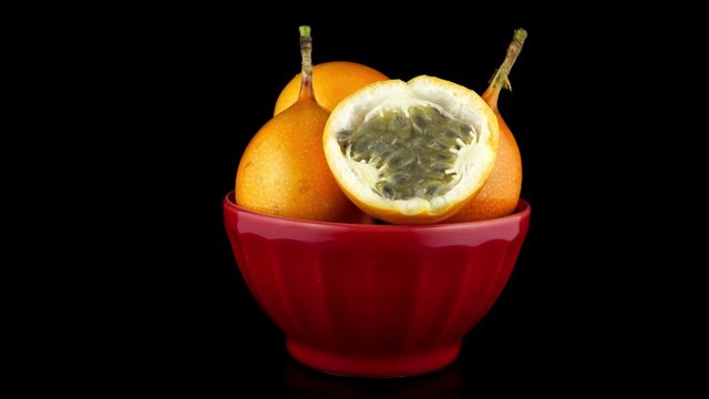 Passion fruit maracuja granadilla on ceramic red bowl, black background.