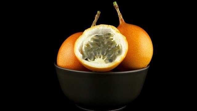 Passion fruit maracuja granadilla on ceramic brown bowl, black background.