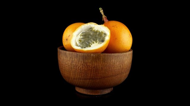Passion fruit maracuja granadilla on wooden bowl, black background.