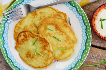 Potato fritters garnished with spring onions and bowl of sour cream on rustic wooden surface
