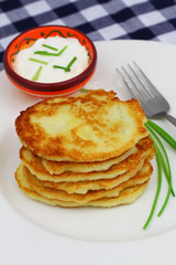 Potato fritters stacked up on white plate and bowl of sour cream

