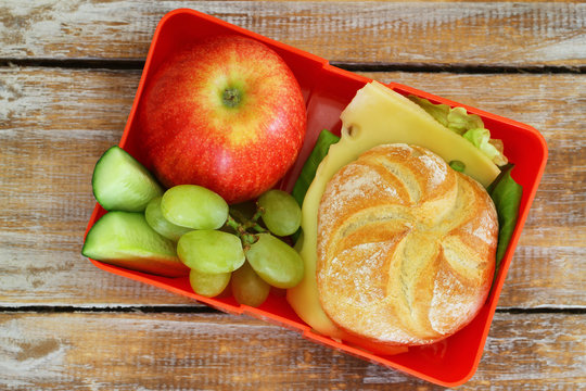 School lunch box containing cheese roll, red apple and grapes
