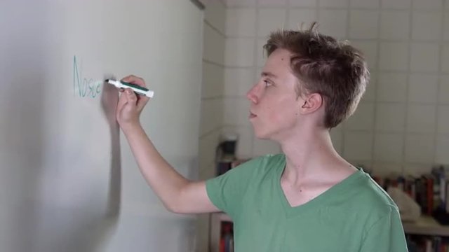 Teenage boy writes "know thyself" in Latin on classroom white board.  Medium close up with small camera dolly.