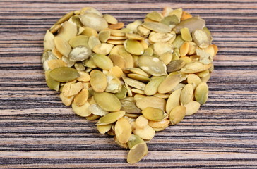 Heart of pumpkin seeds on wooden background